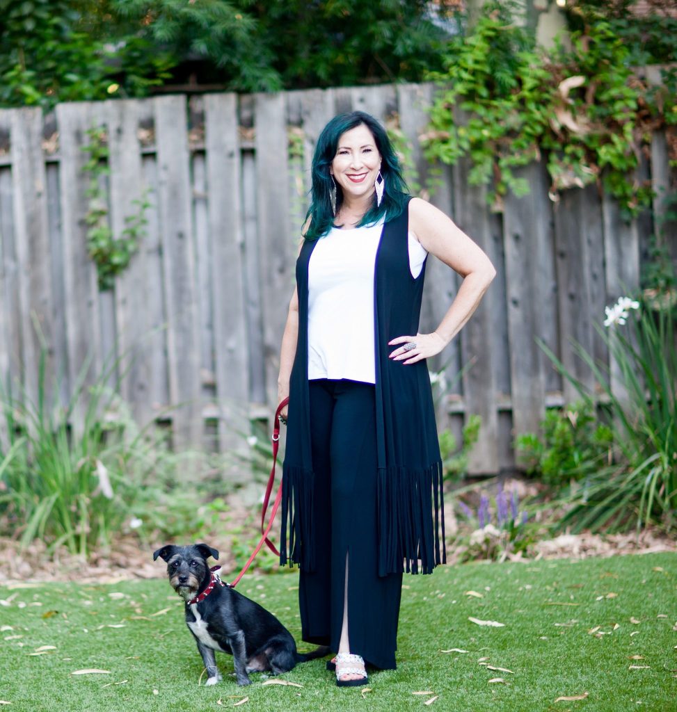 Woman in a fringed vest holding her dog on her leash. 